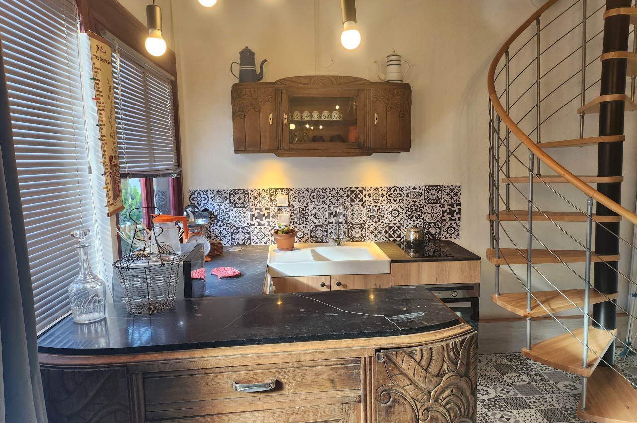 Cuisine avec meubles en bois sculpté, plan de travail en marbre, carrelage décoratif et escalier en colimaçon.