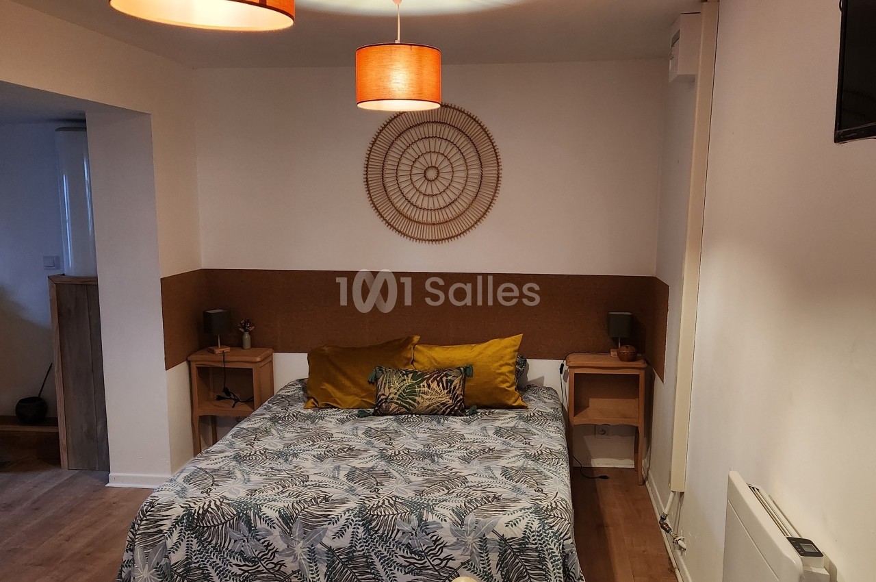Chambre avec lit double, linge à motifs végétaux, coussins colorés, décor mural en rotin et éclairage suspendu.