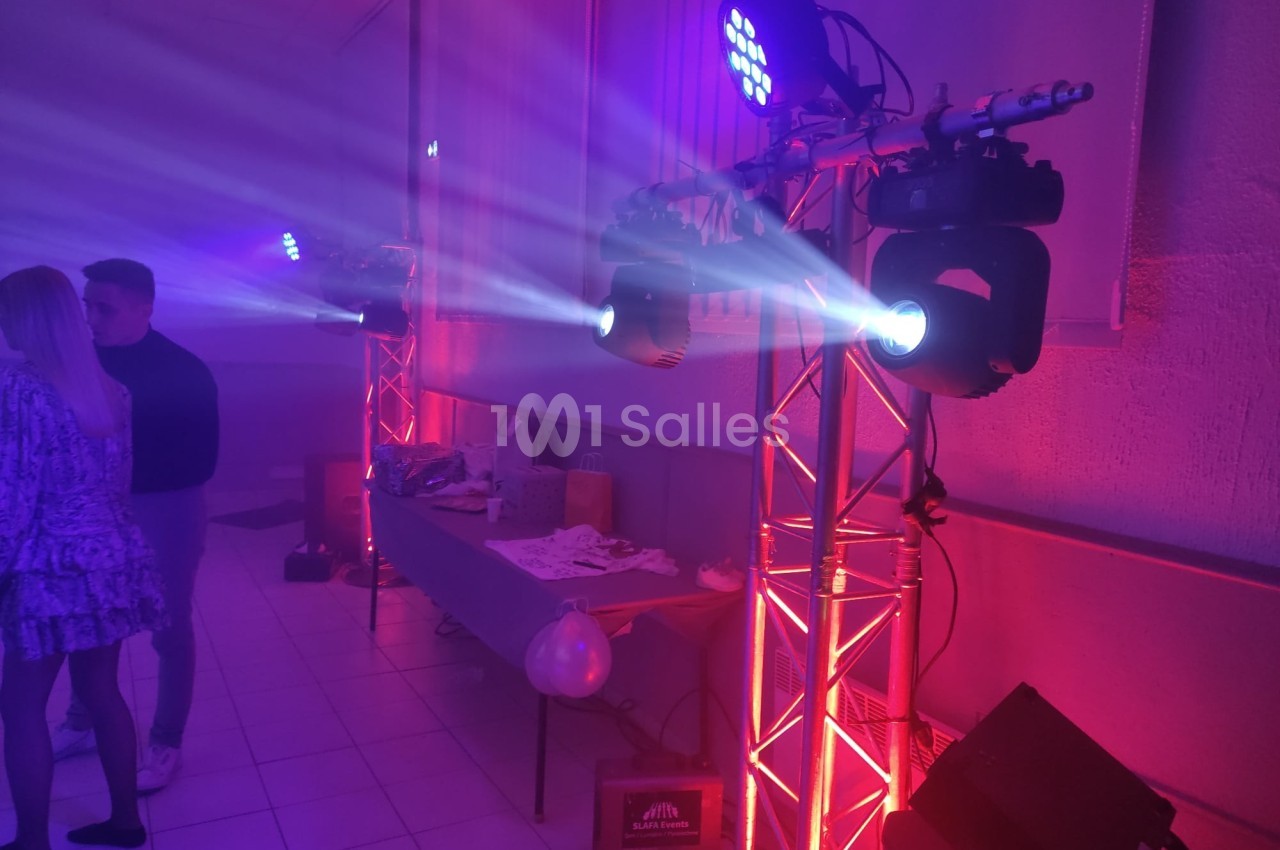 Projecteurs LED colorés éclairant une salle avec des tables décorées et des invités en arrière-plan.