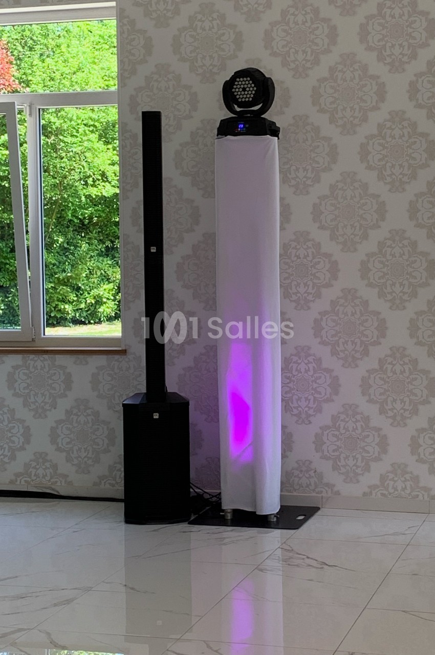 Système de sonorisation avec haut-parleur et éclairage LED violet, placé dans une pièce lumineuse avec sol en marbre.