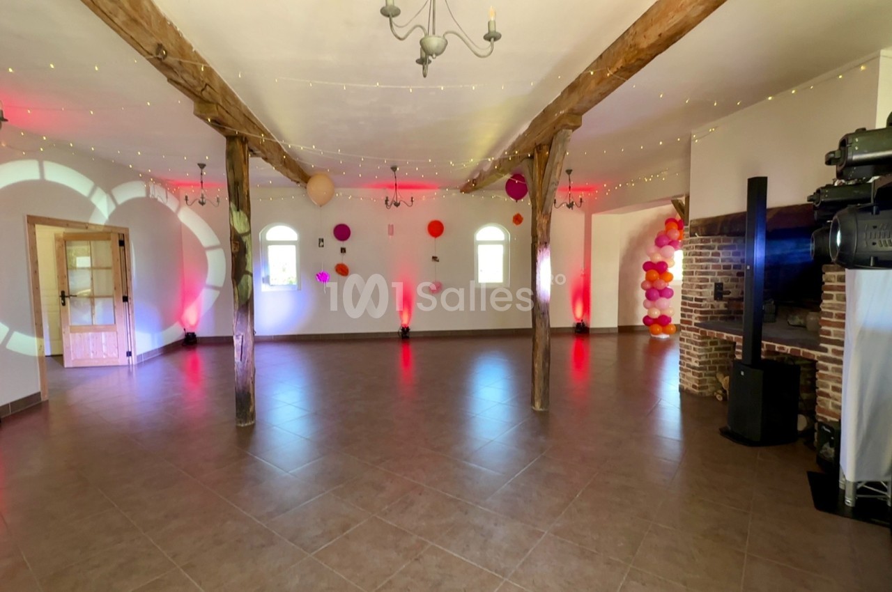 Salle spacieuse décorée de guirlandes lumineuses, ballons colorés et éclairages rouges, avec poutres apparentes.