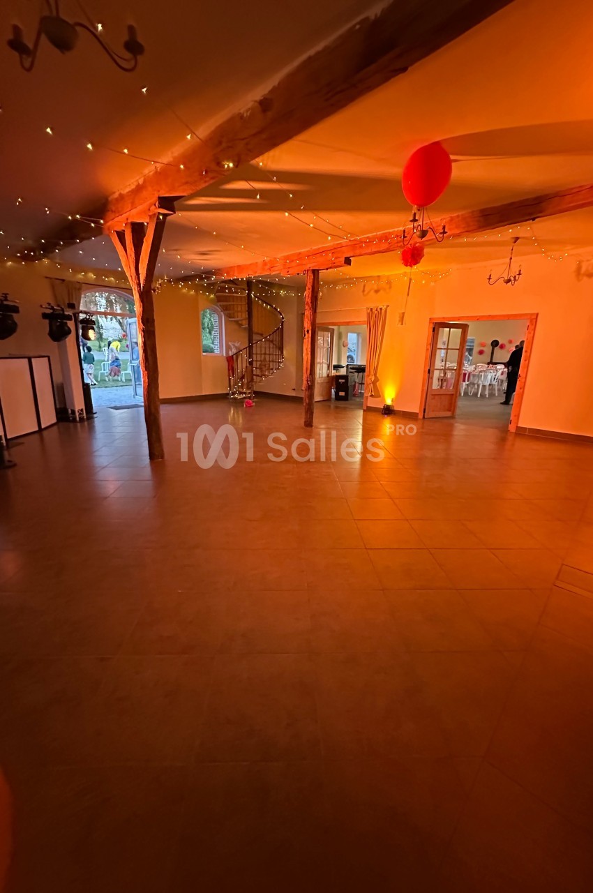 Salle spacieuse avec poutres apparentes, éclairage chaleureux, décorations lumineuses et ballon rouge suspendu.