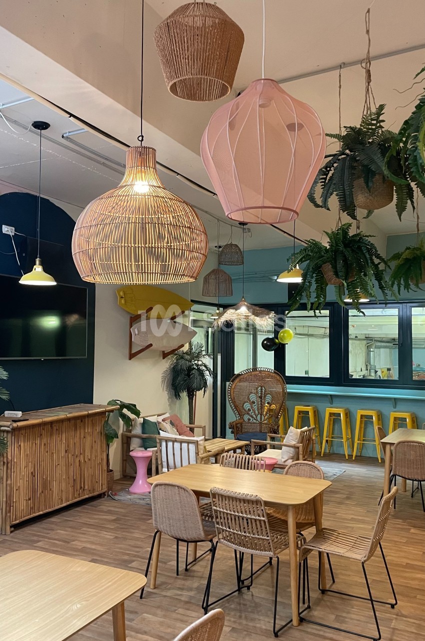 Espace intérieur lumineux avec mobilier en bois, suspensions en osier, plantes suspendues et comptoir en bambou.