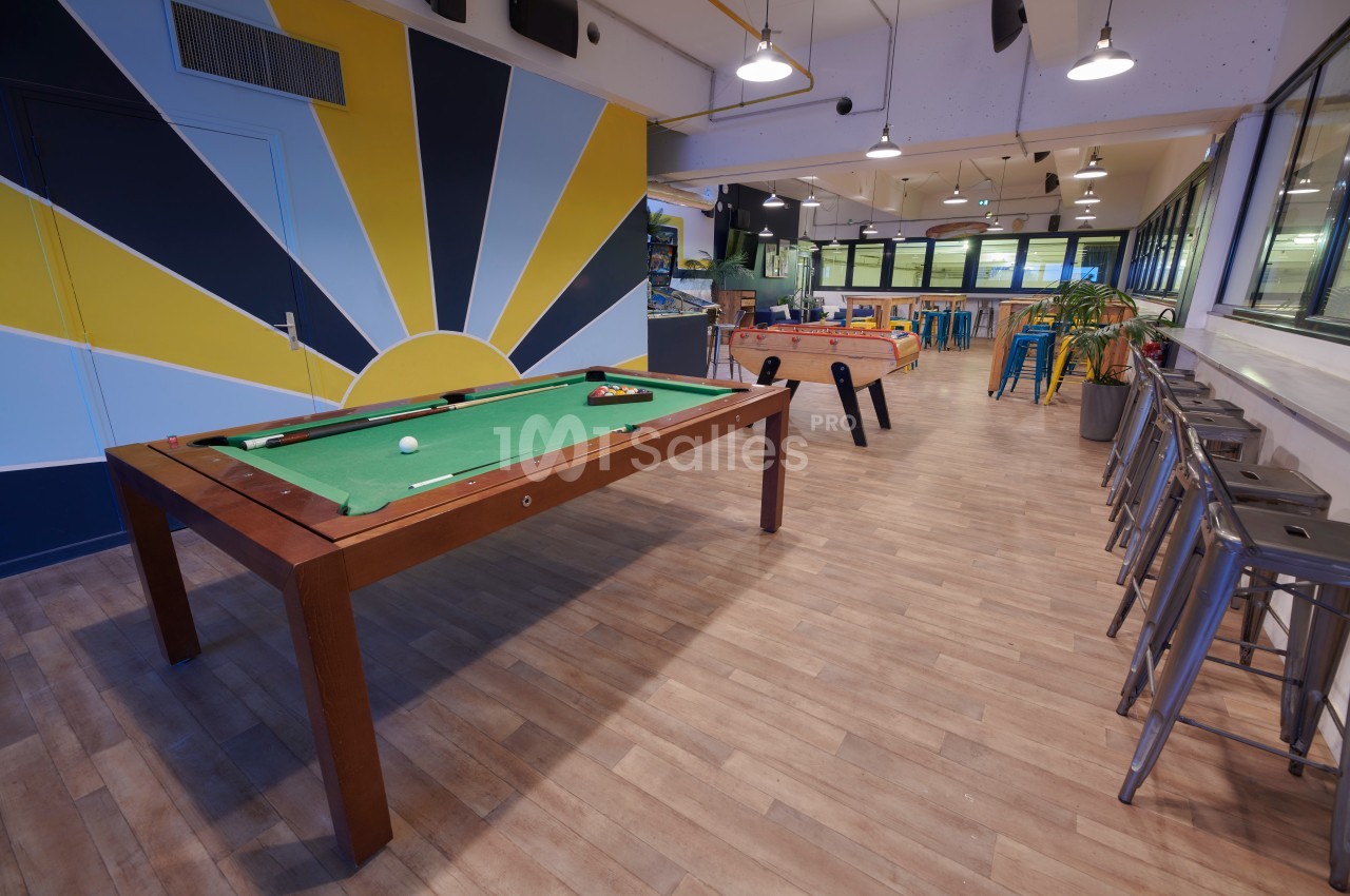 Salle de détente avec une table de billard, un baby-foot, des tabourets hauts et un décor coloré.