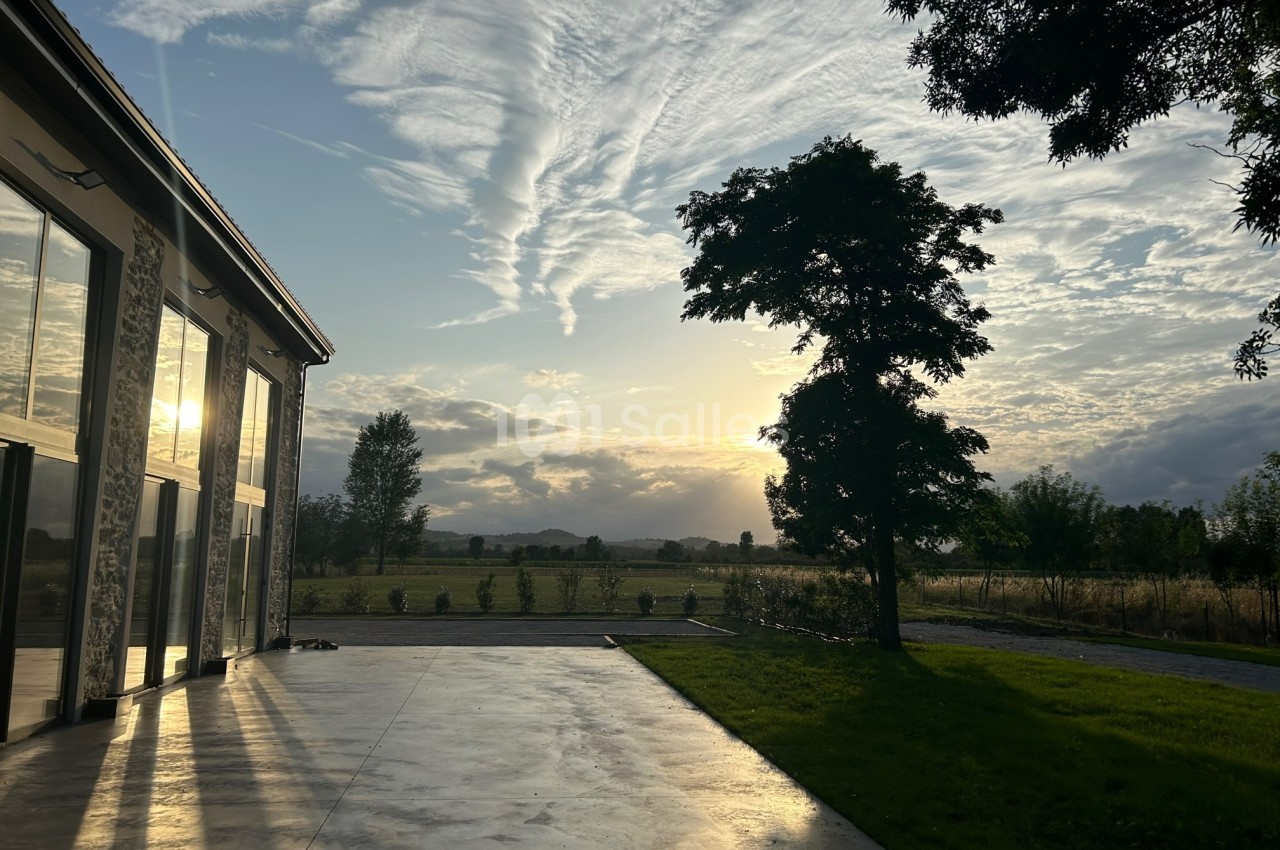 Coucher de soleil illuminant une terrasse en béton, avec un arbre et un paysage champêtre en arrière-plan.