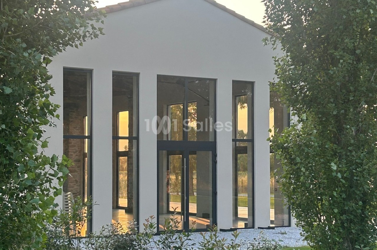 Façade d'une maison moderne avec de grandes baies vitrées, entourée de verdure et éclairée par une lumière douce.