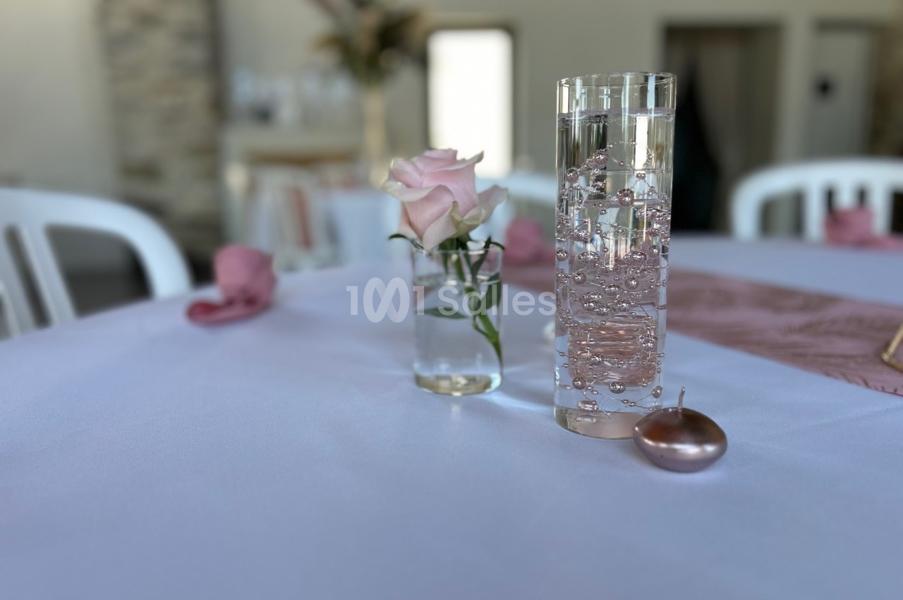 Vase avec une rose rose et verre d'eau pétillant sur une table blanche décorée de serviettes roses.