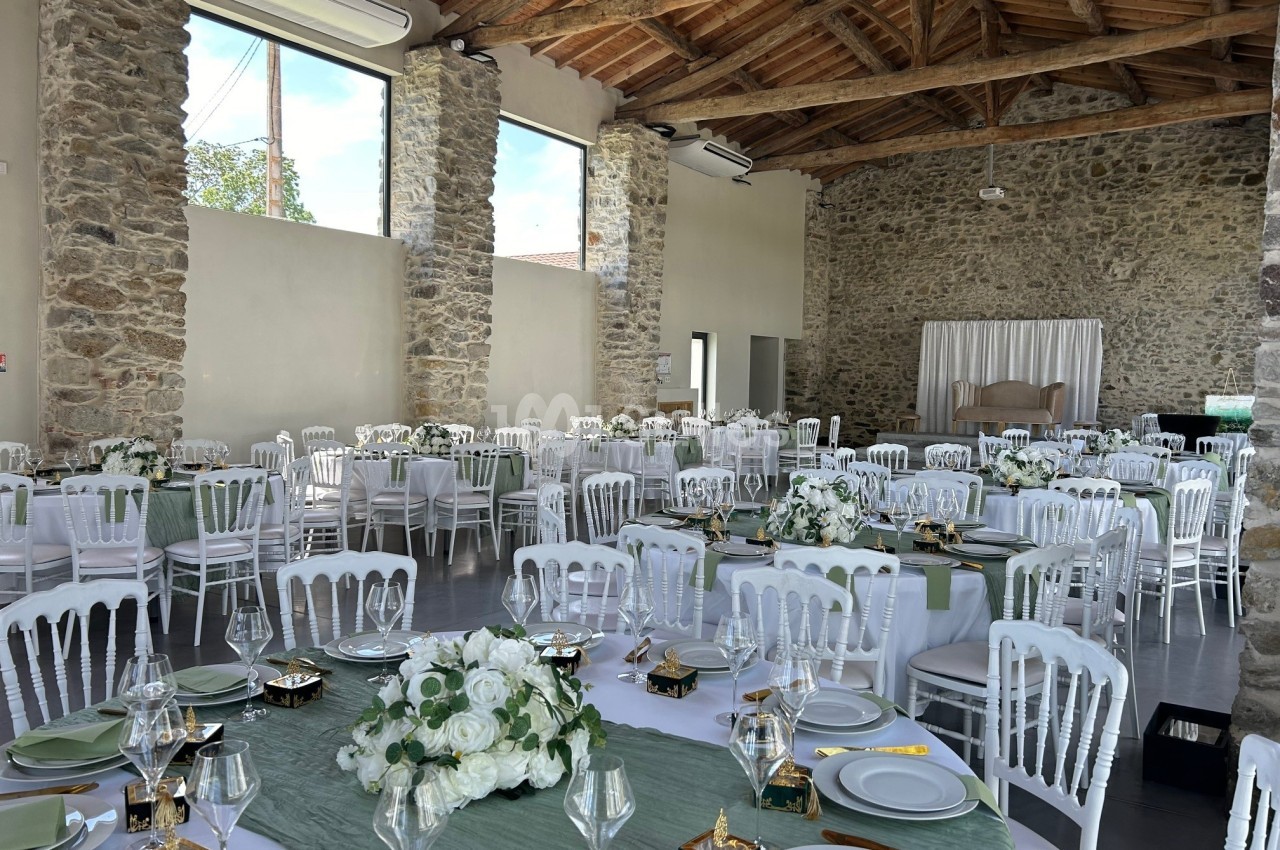 Salle de réception décorée pour un événement, avec tables dressées, nappes vertes et arrangements floraux blancs.