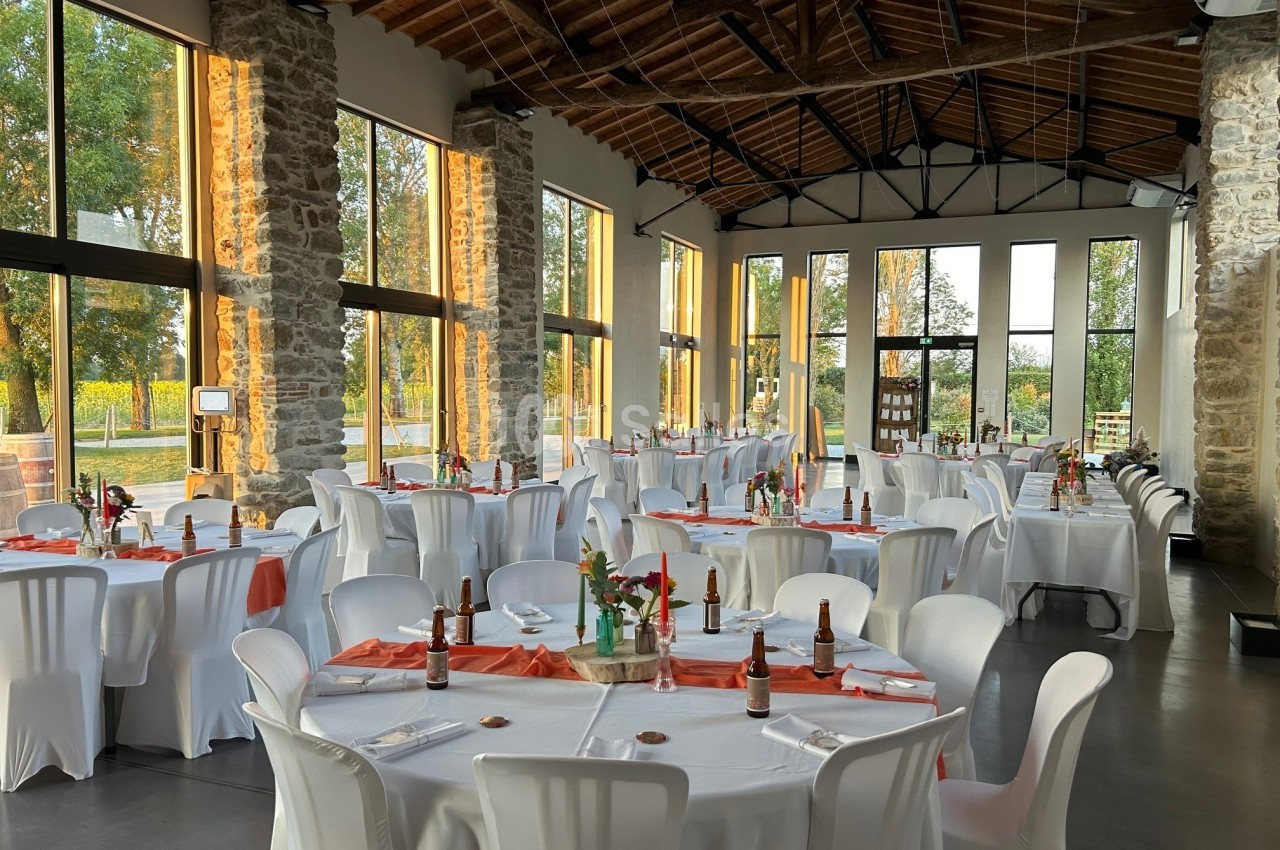 Salle de réception lumineuse avec des tables rondes dressées, nappes blanches et décorations florales.