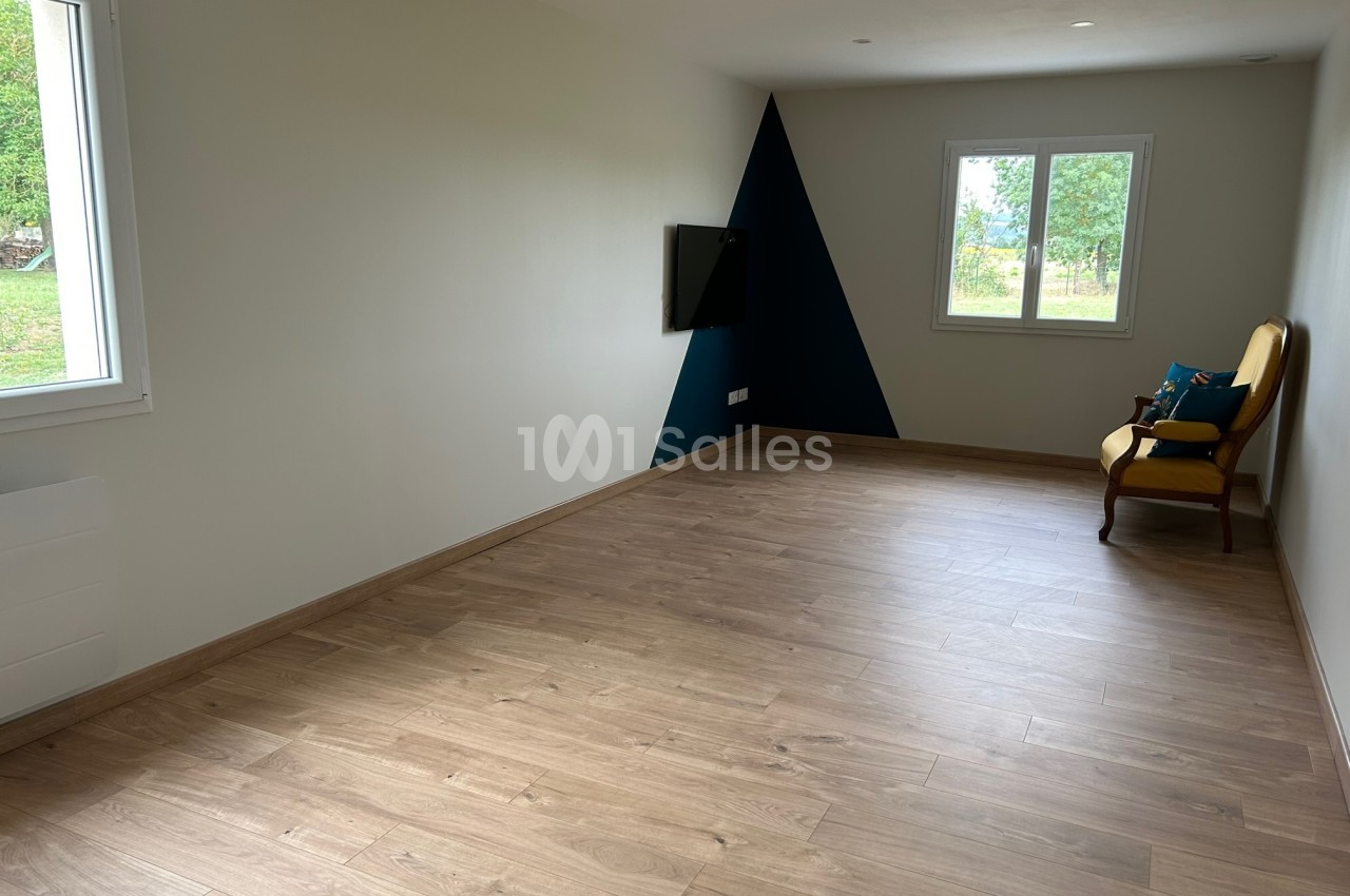 Salle lumineuse avec parquet en bois, mur blanc et bleu, fenêtre donnant sur un jardin, fauteuil jaune contre le mur.