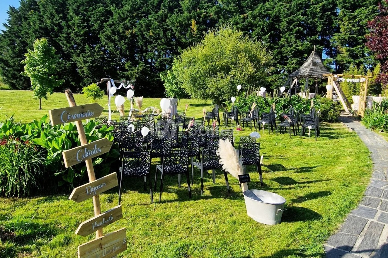 Chaises noires alignées en extérieur pour une cérémonie, avec panneaux directionnels et décorations sur une pelouse…