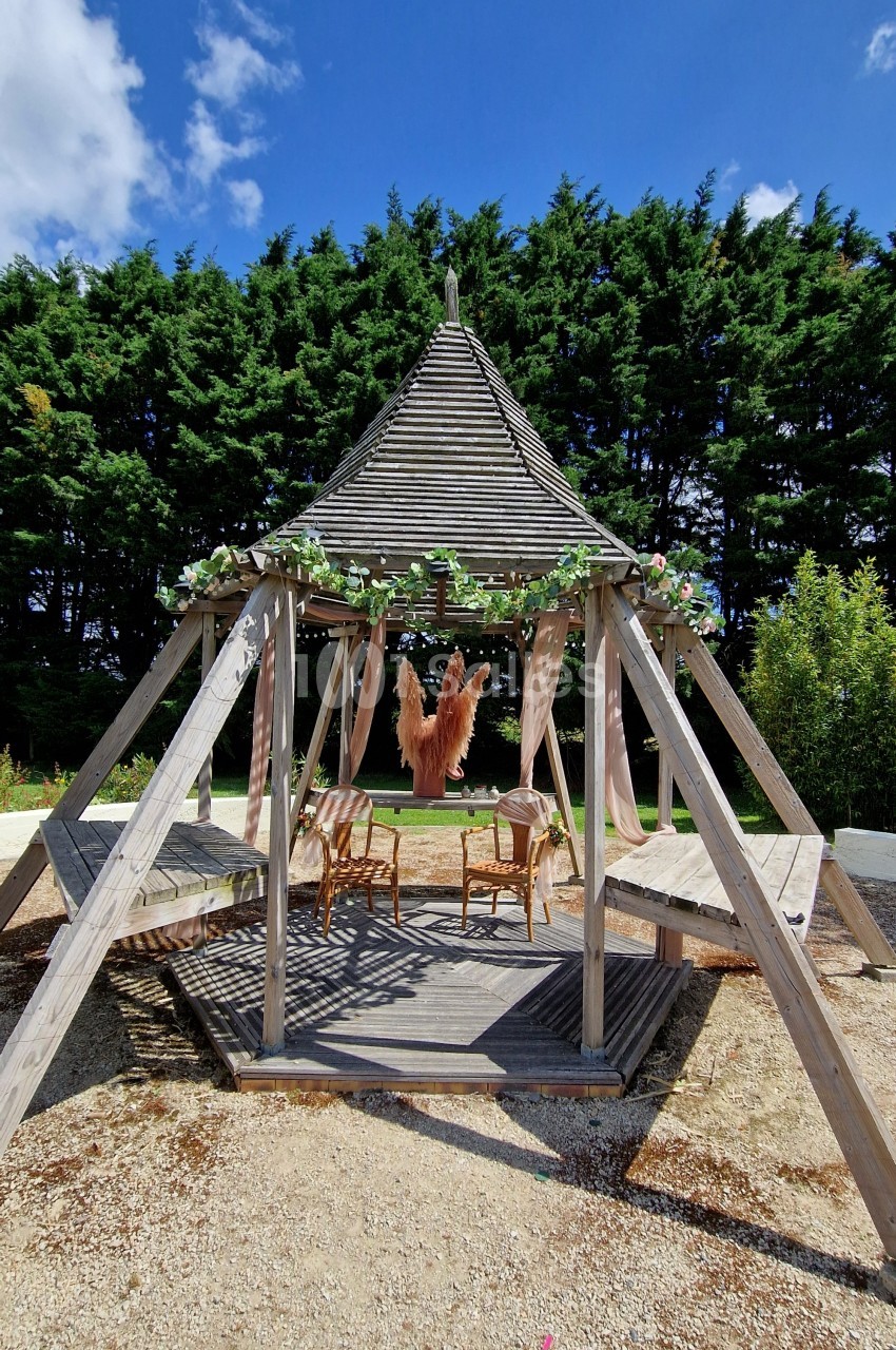 Structure en bois avec toit en pointe, décorée de guirlandes, abritant des chaises sur une terrasse ensoleillée.