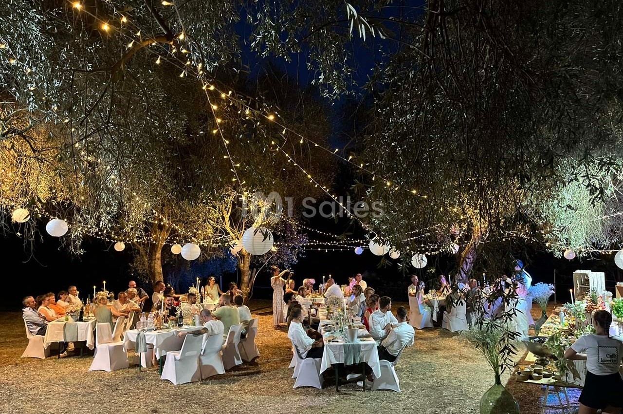 Dîner en plein air sous des guirlandes lumineuses et lanternes, avec des invités assis à des tables décorées.