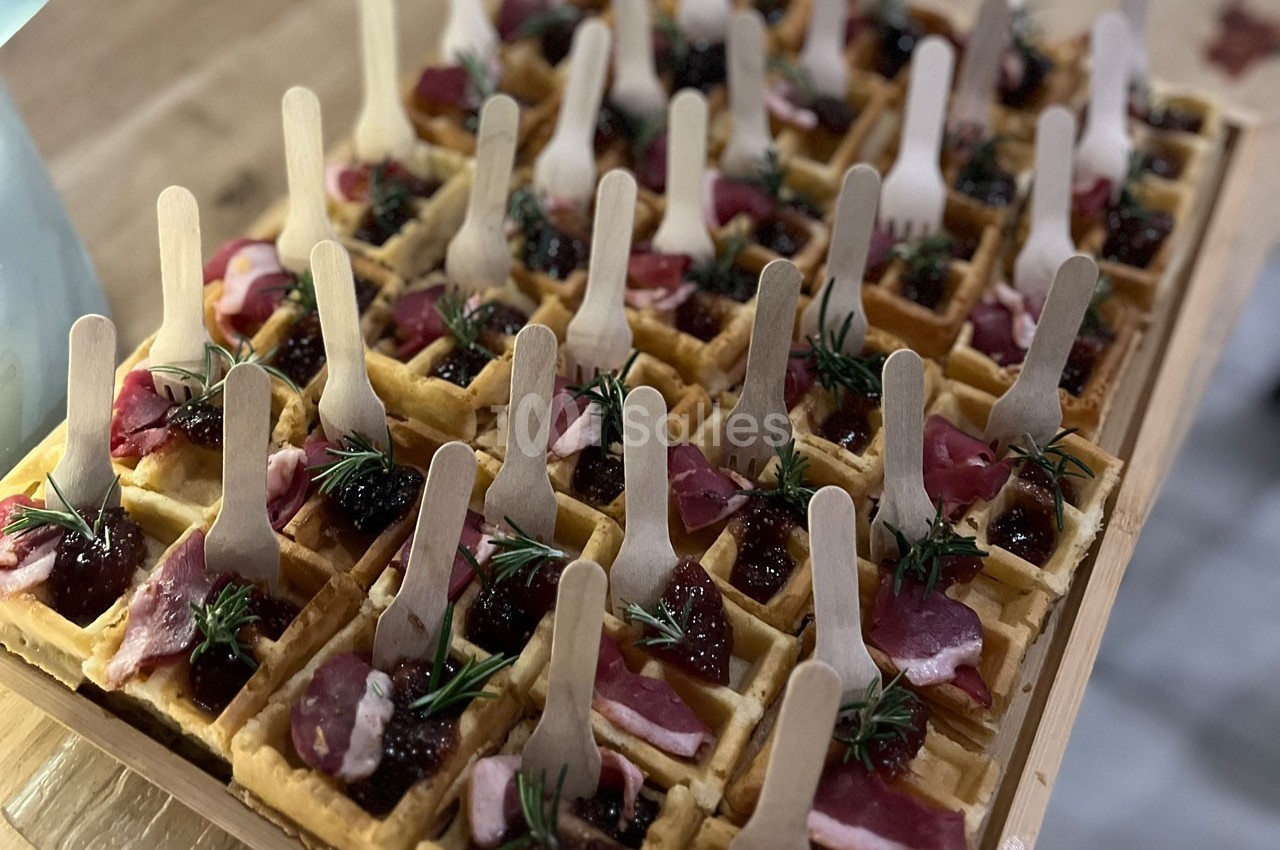 Plateau de mini-gaufres garnies de viande séchée, confiture et brins de romarin, avec des fourchettes en bois.