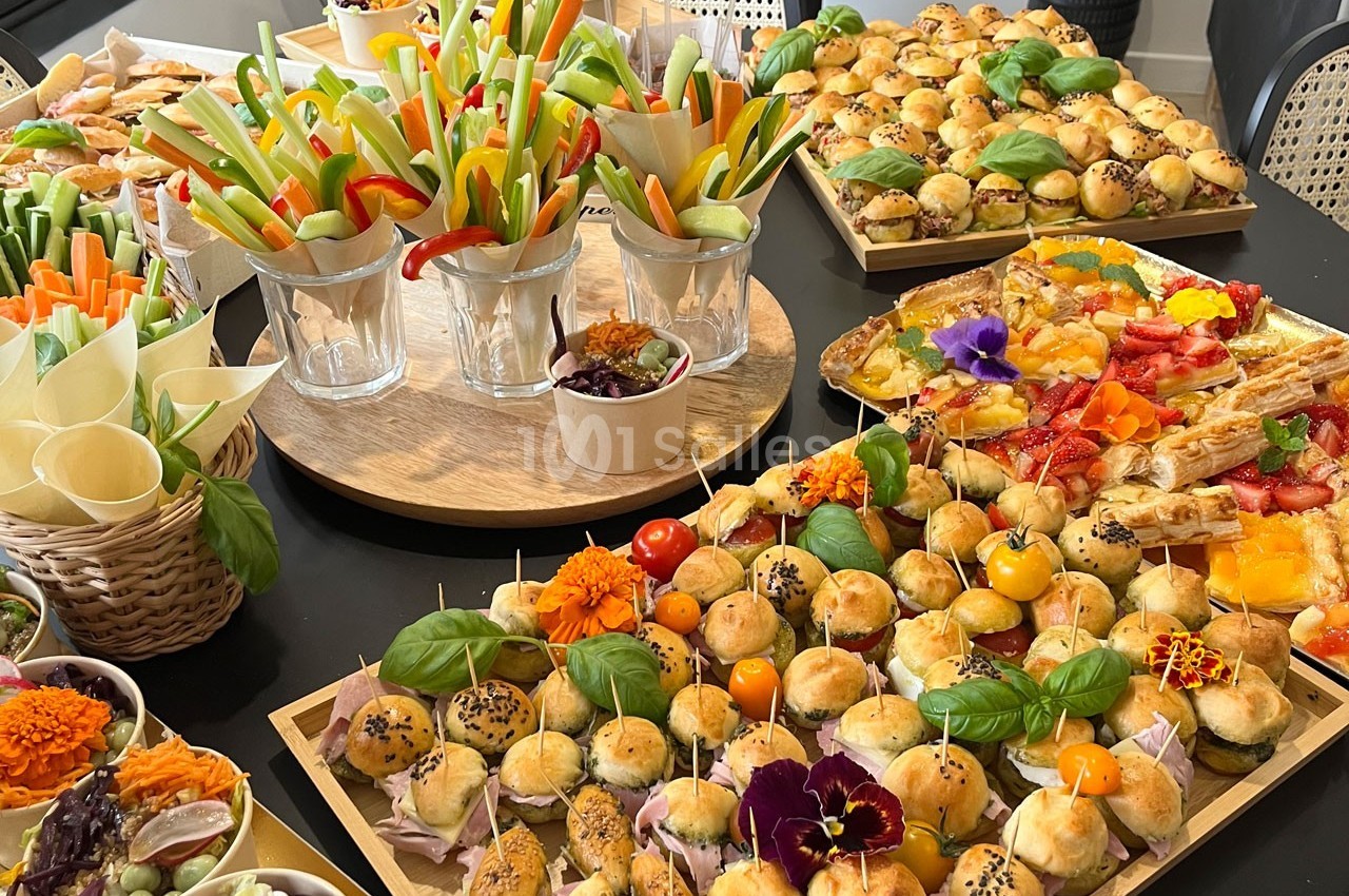 Plateau de buffet avec des amuse-bouches variés, légumes croquants, mini-sandwichs et décorations florales comestibles.