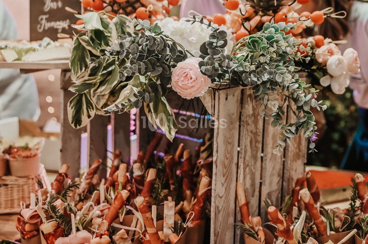 Présentoir décoré avec des fleurs et des plantes, entouré de cornets garnis de charcuterie et de fromage.