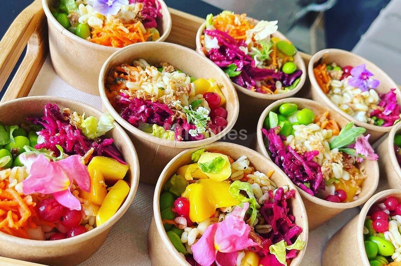 Assortiment de bols en carton contenant des salades colorées garnies de légumes, fruits et fleurs comestibles.