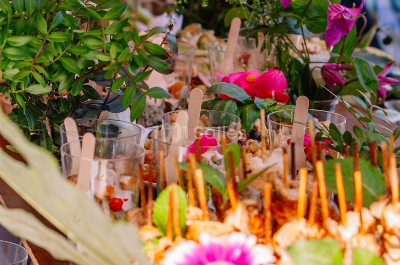 Buffet coloré avec verrines garnies et décorations florales entourées de feuillage vert.