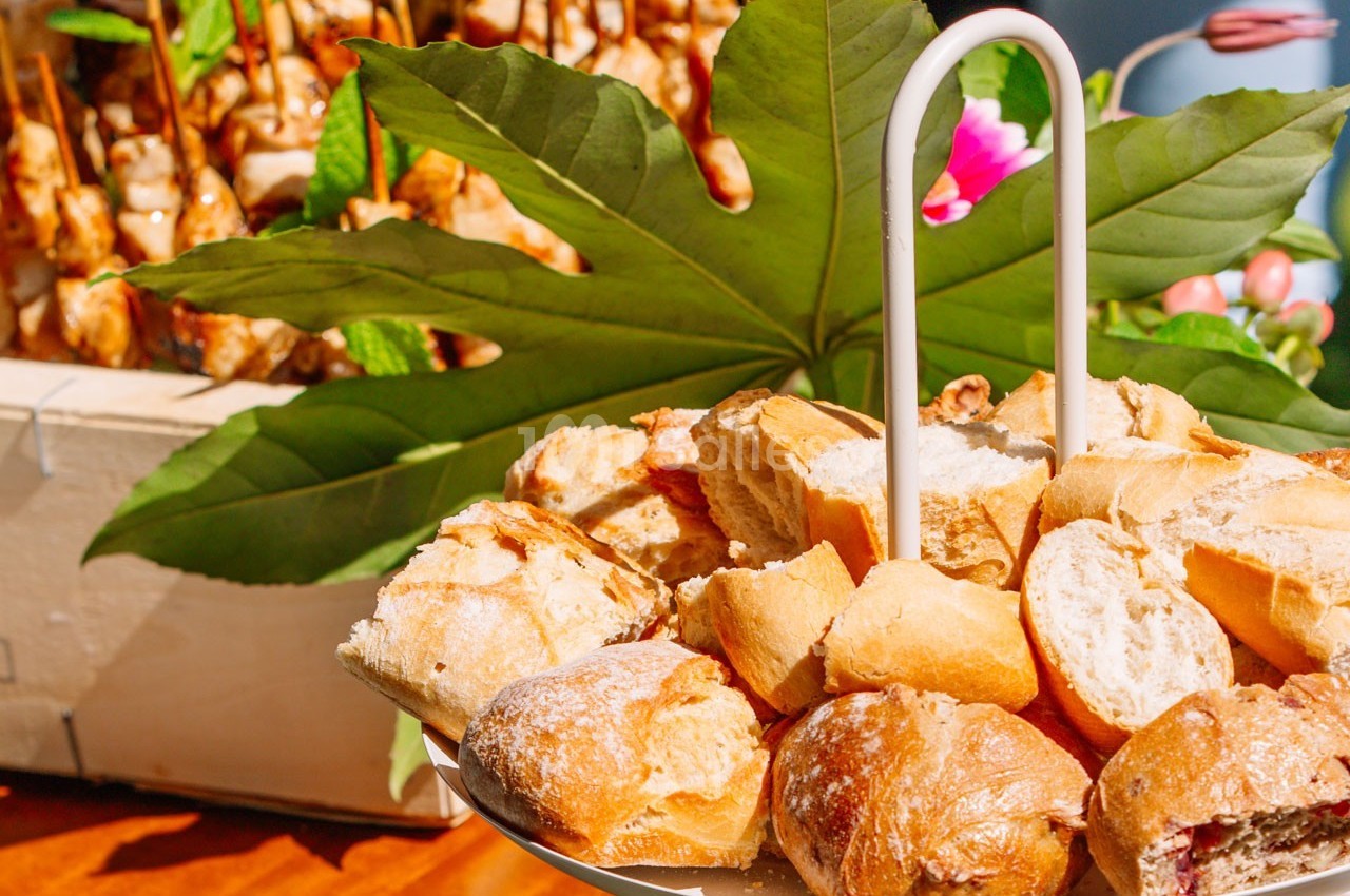 Assortiment de petits pains sur un plateau, avec des brochettes en arrière-plan et une grande feuille décorative.