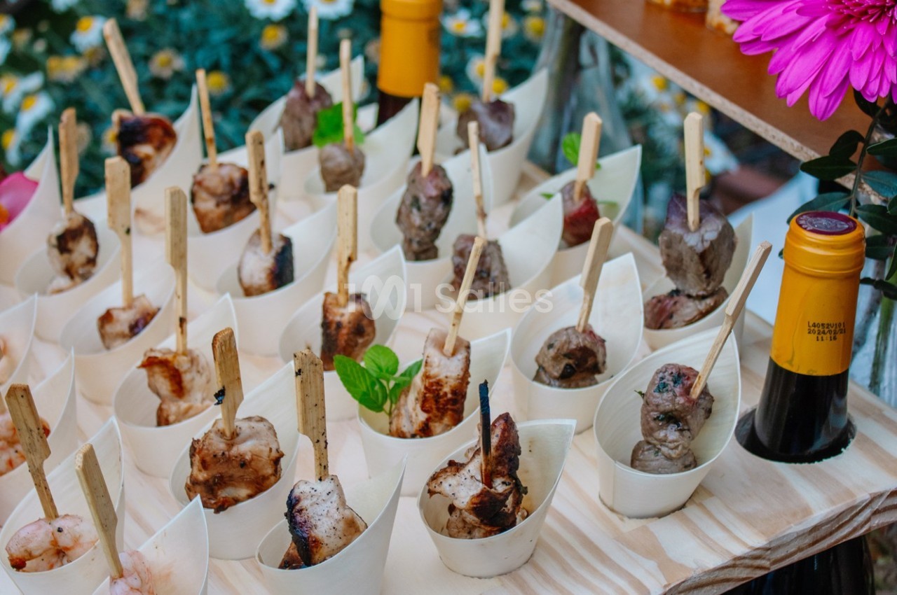 Brochettes de viande et fruits de mer présentées dans des coupelles individuelles sur une table en bois.