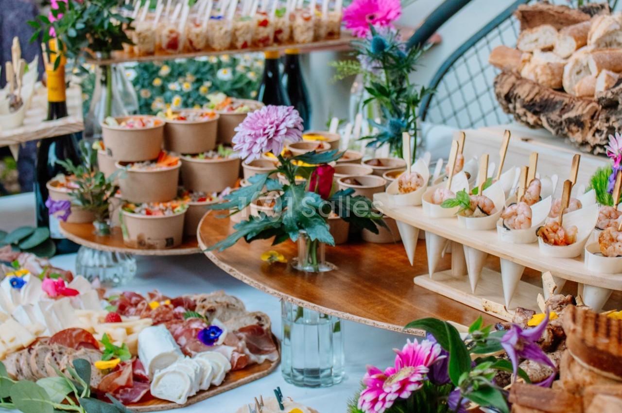 Buffet coloré avec des plats variés, incluant des verrines, des cônes apéritifs et des fleurs décoratives.