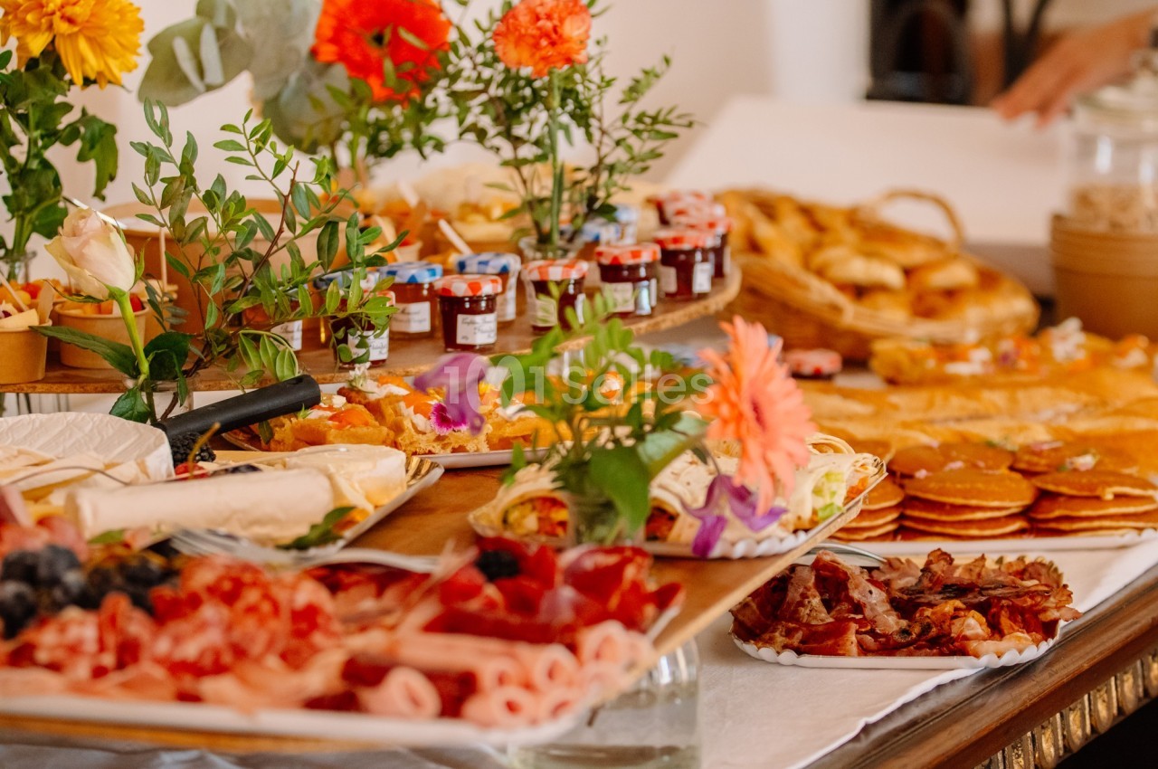 Table garnie de plats variés, incluant charcuterie, crêpes, viennoiseries, confitures et décorations florales.