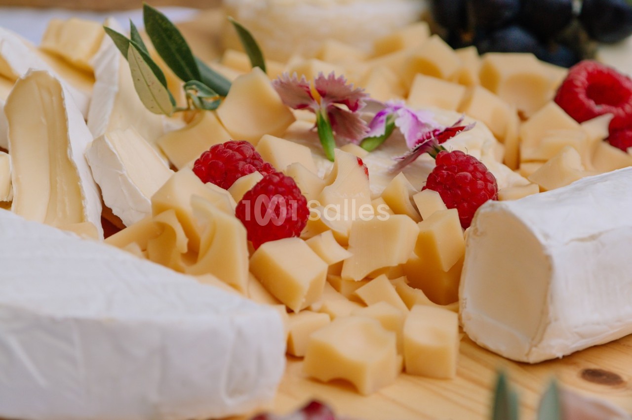 Assortiment de fromages variés avec framboises, fleurs décoratives et olives sur une planche en bois.