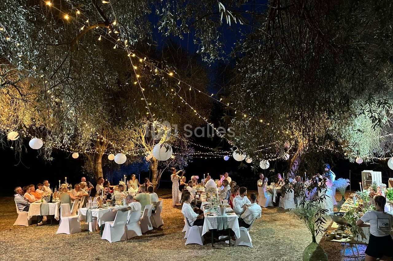 Dîner en plein air sous des guirlandes lumineuses et lanternes, avec des invités assis à des tables décorées.
