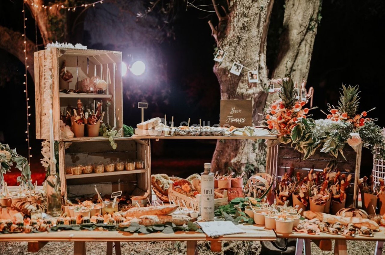 Buffet rustique en extérieur avec étals en bois, décorations florales et mets variés sous un éclairage chaleureux.