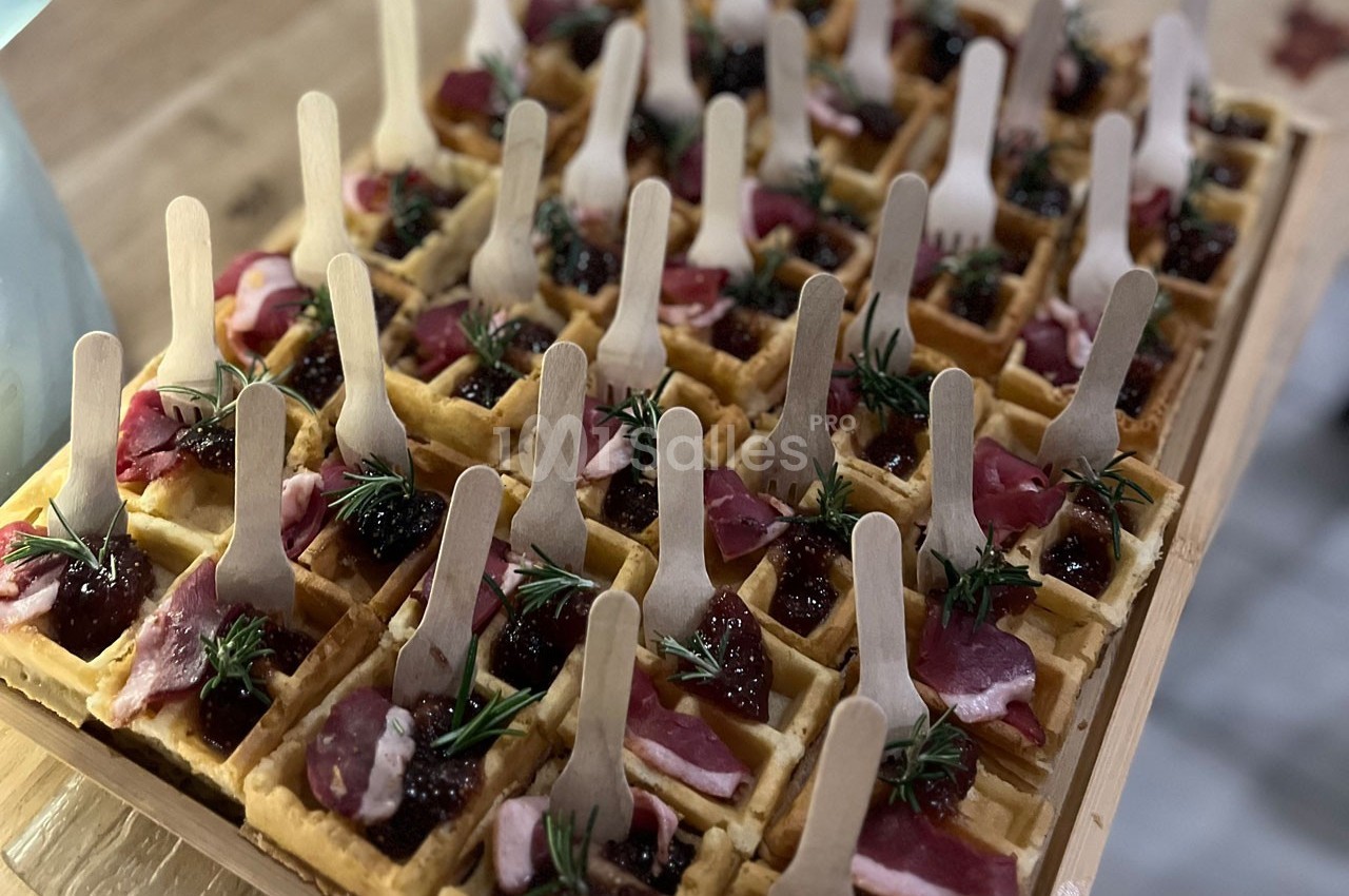 Plateau de mini-gaufres garnies de viande séchée, confiture et brins de romarin, avec des fourchettes en bois.