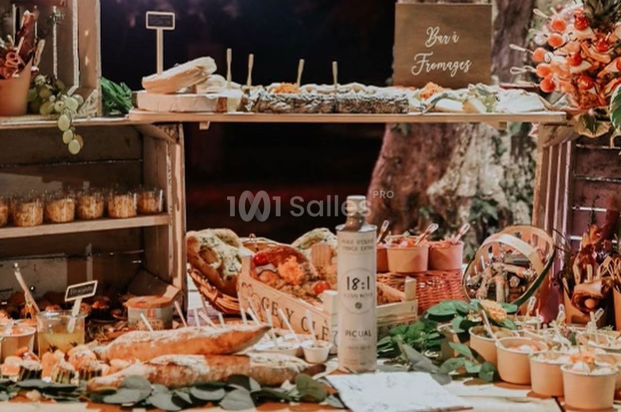Buffet rustique en extérieur avec fromages, pains, fruits et condiments, décoré de feuillages et d'éléments en bois.