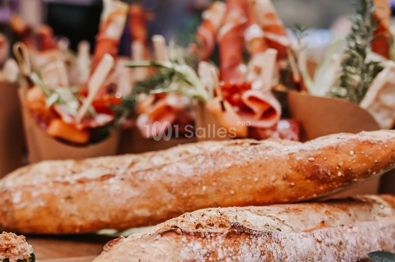 Deux baguettes de pain croustillantes au premier plan, avec des amuse-bouches à base de charcuterie en arrière-plan.