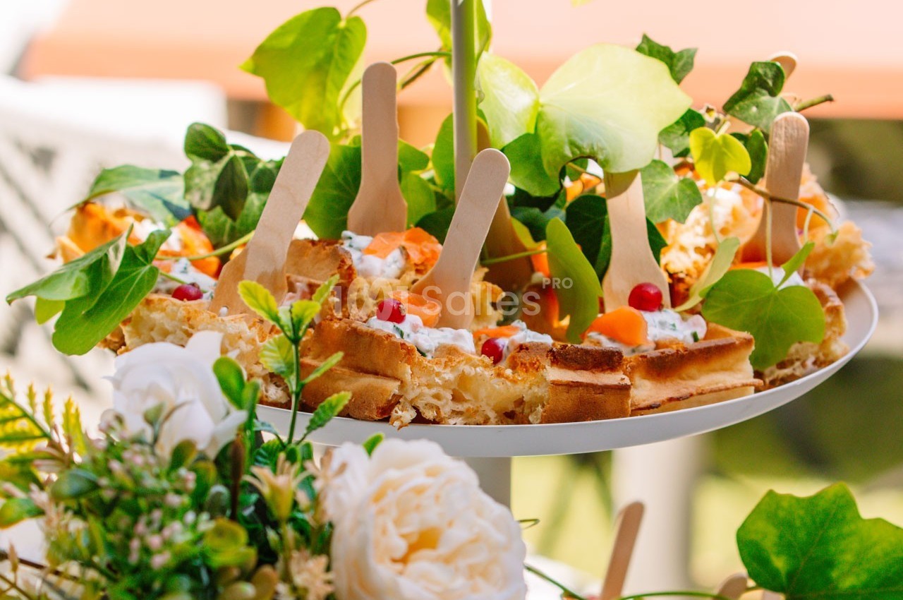 Assiette garnie de gaufres décorées de fruits et de crème, entourée de feuillage et de fleurs.