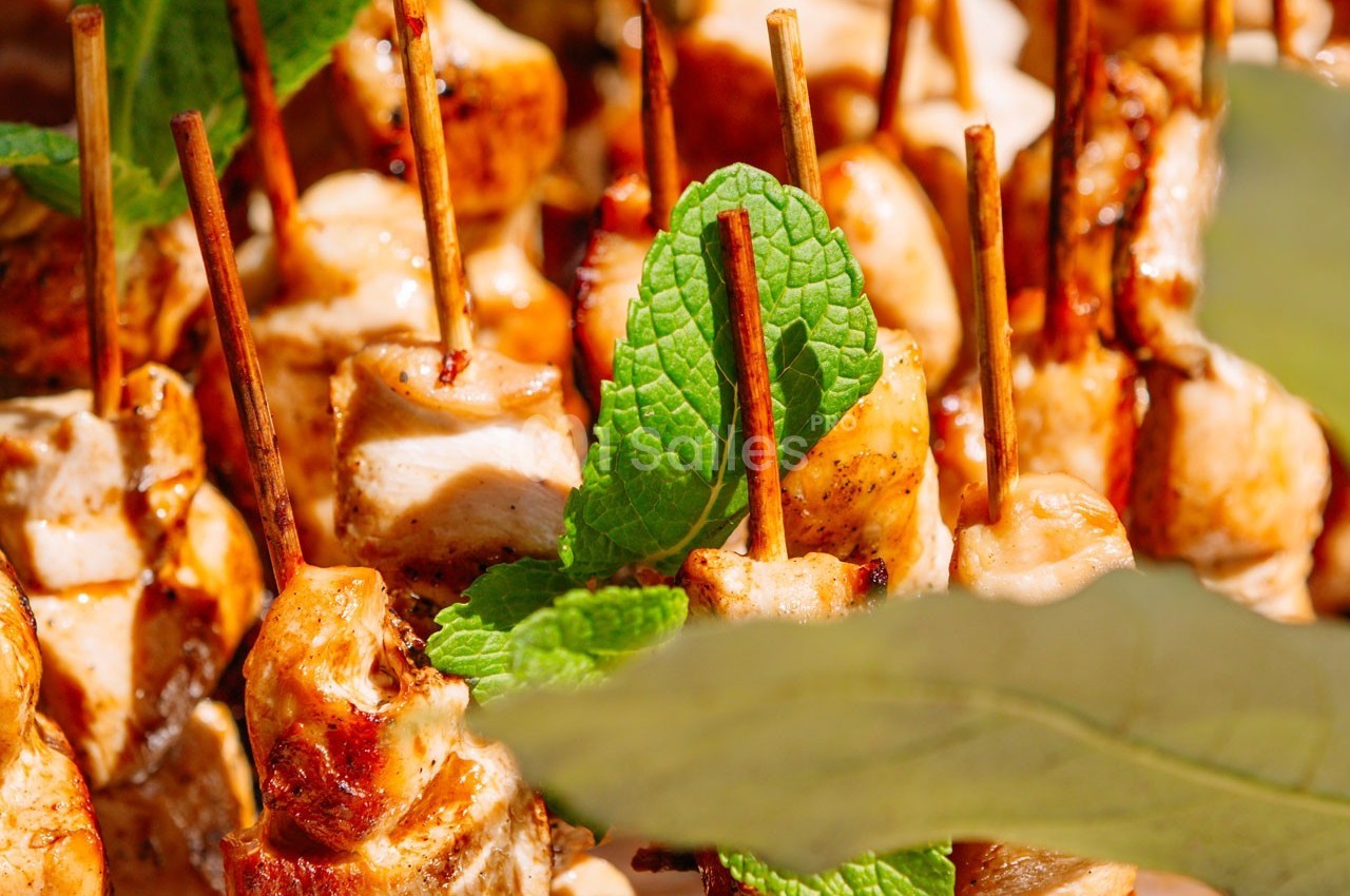 Brochettes de poulet grillé garnies de feuilles de menthe, présentées sur un plateau en plein air.