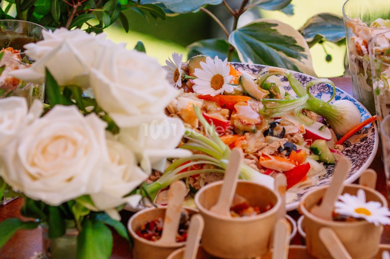 Assiette garnie de légumes colorés et petits plats en bois, entourés de fleurs blanches et de verdure.