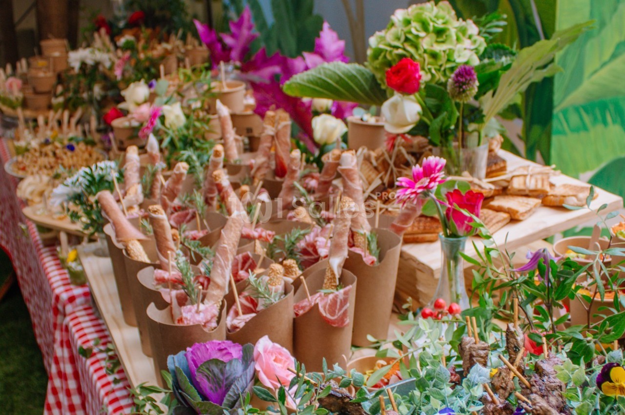 Table garnie de fleurs colorées et de mets variés présentés dans des contenants en carton, ambiance festive et naturelle.