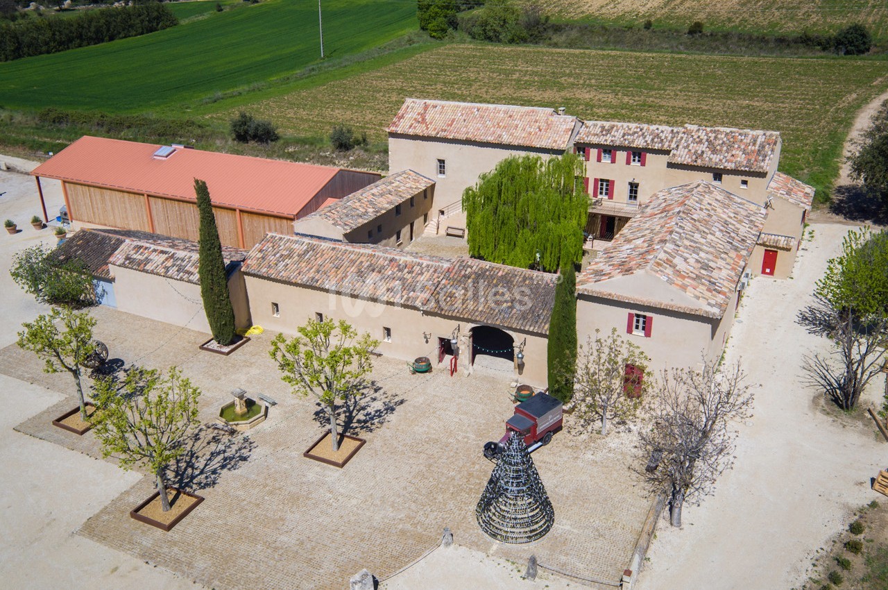Vue aérienne d'un domaine rural avec bâtiments en pierre, cour pavée, arbres et champs environnants.