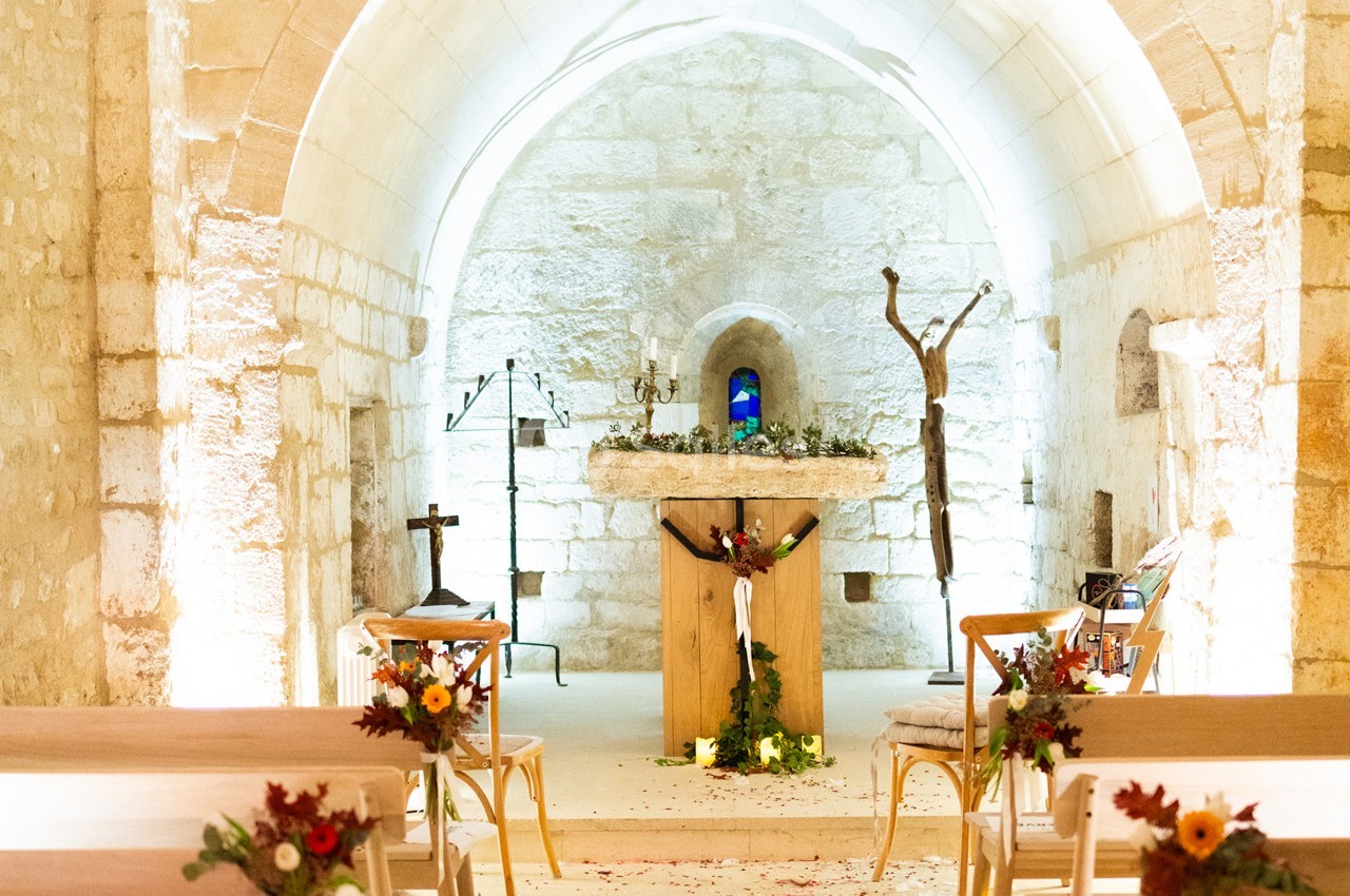 Intérieur d'une chapelle en pierre avec un autel décoré de fleurs et des bancs alignés pour une cérémonie.