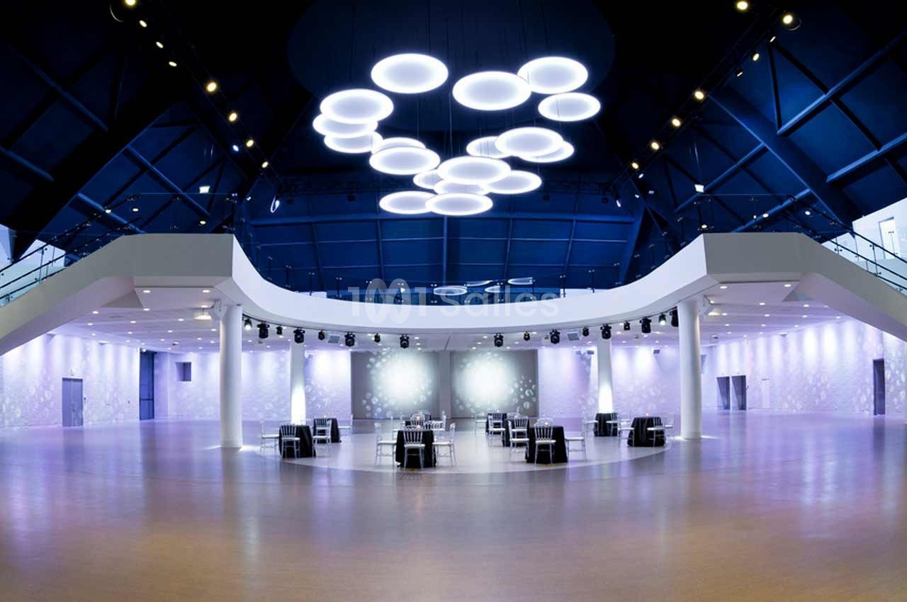 Salle spacieuse et moderne avec un plafond bleu, des luminaires circulaires suspendus et des tables dispersées.