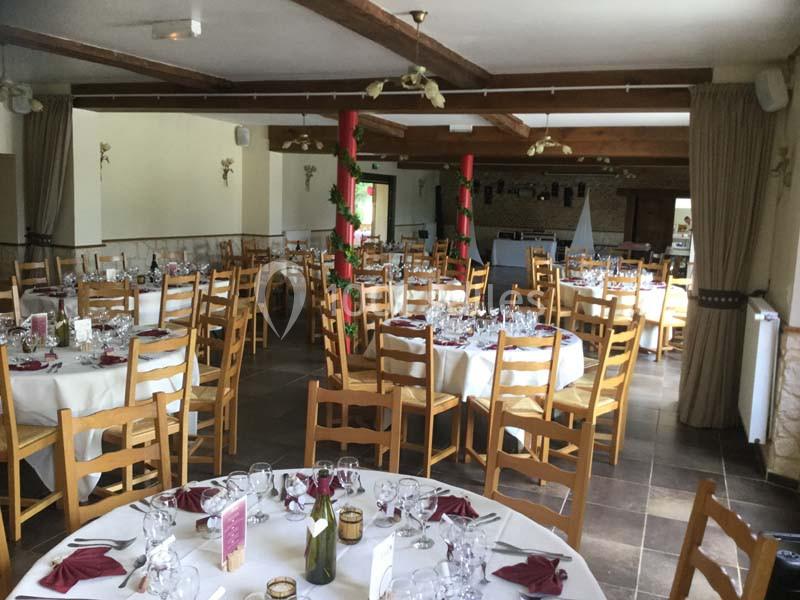 Salle de réception décorée avec des tables rondes dressées, nappes blanches et serviettes rouges, ambiance lumineuse.