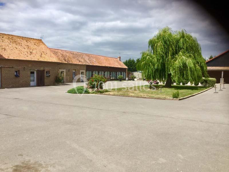 Cour pavée avec un bâtiment en briques, un toit en tuiles, un saule pleureur et des espaces verts aménagés.