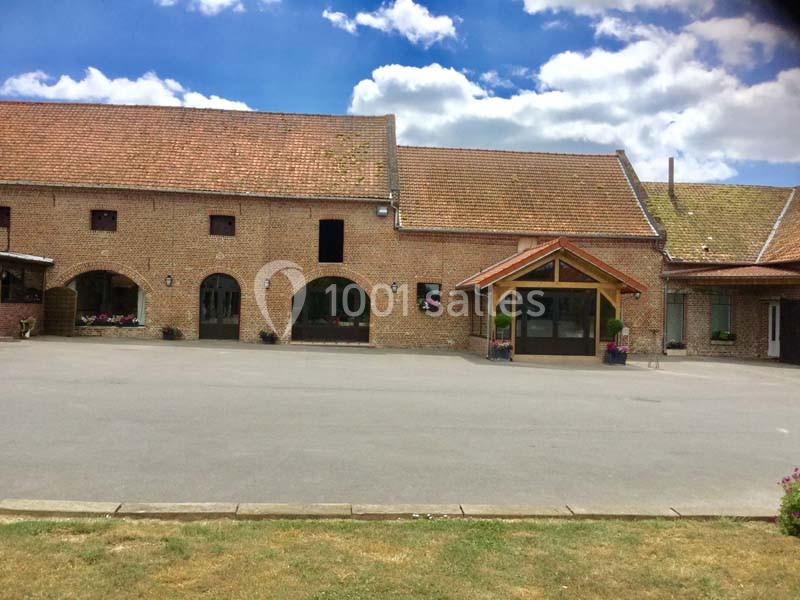 Bâtiment en briques avec toit en tuiles, grandes fenêtres et entrée couverte, entouré d'une cour pavée.