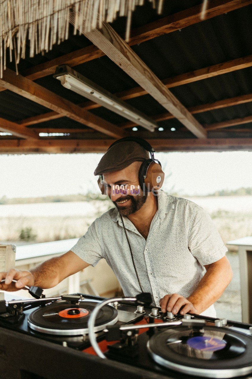 Un homme souriant mixe des disques vinyles sur une platine sous un abri en bois.