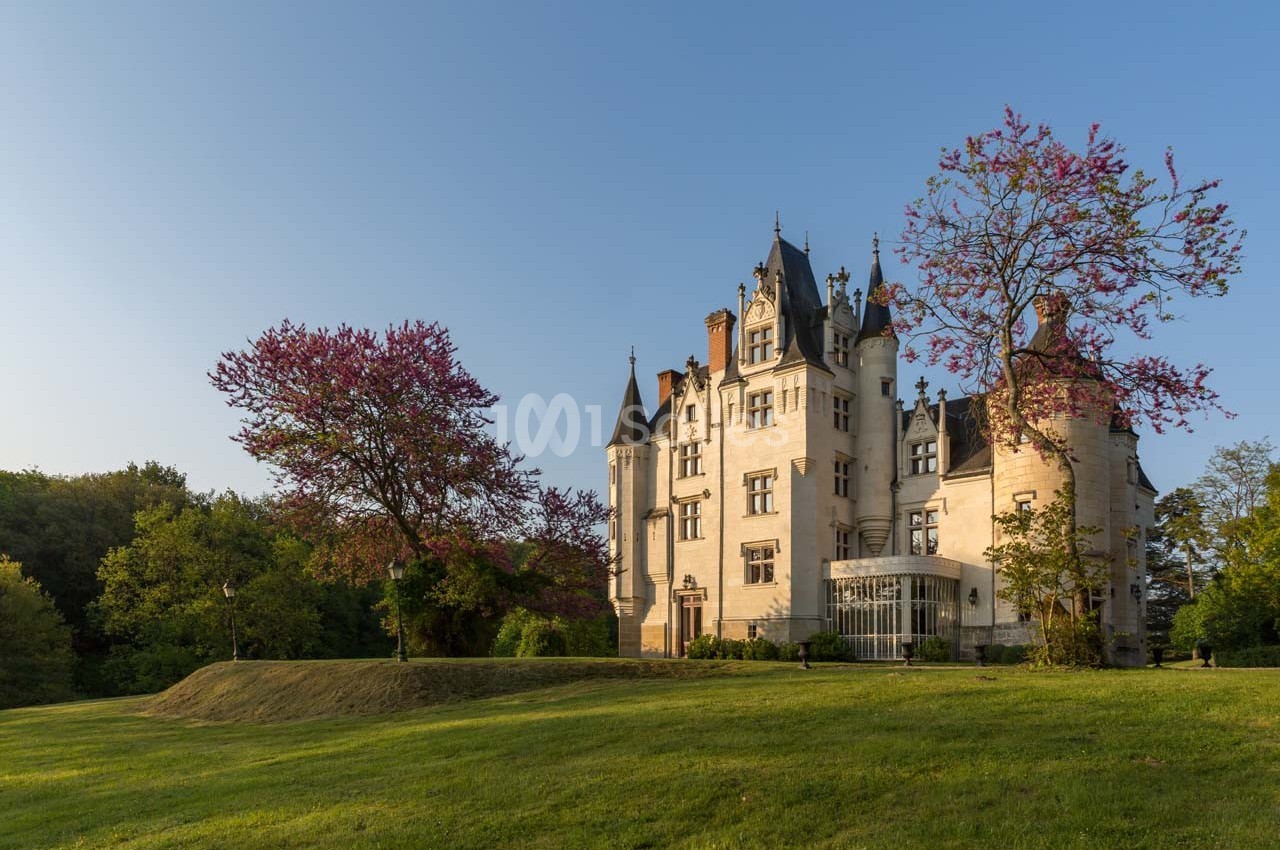 Château entouré d'un parc verdoyant avec des arbres en fleurs sous un ciel dégagé.
