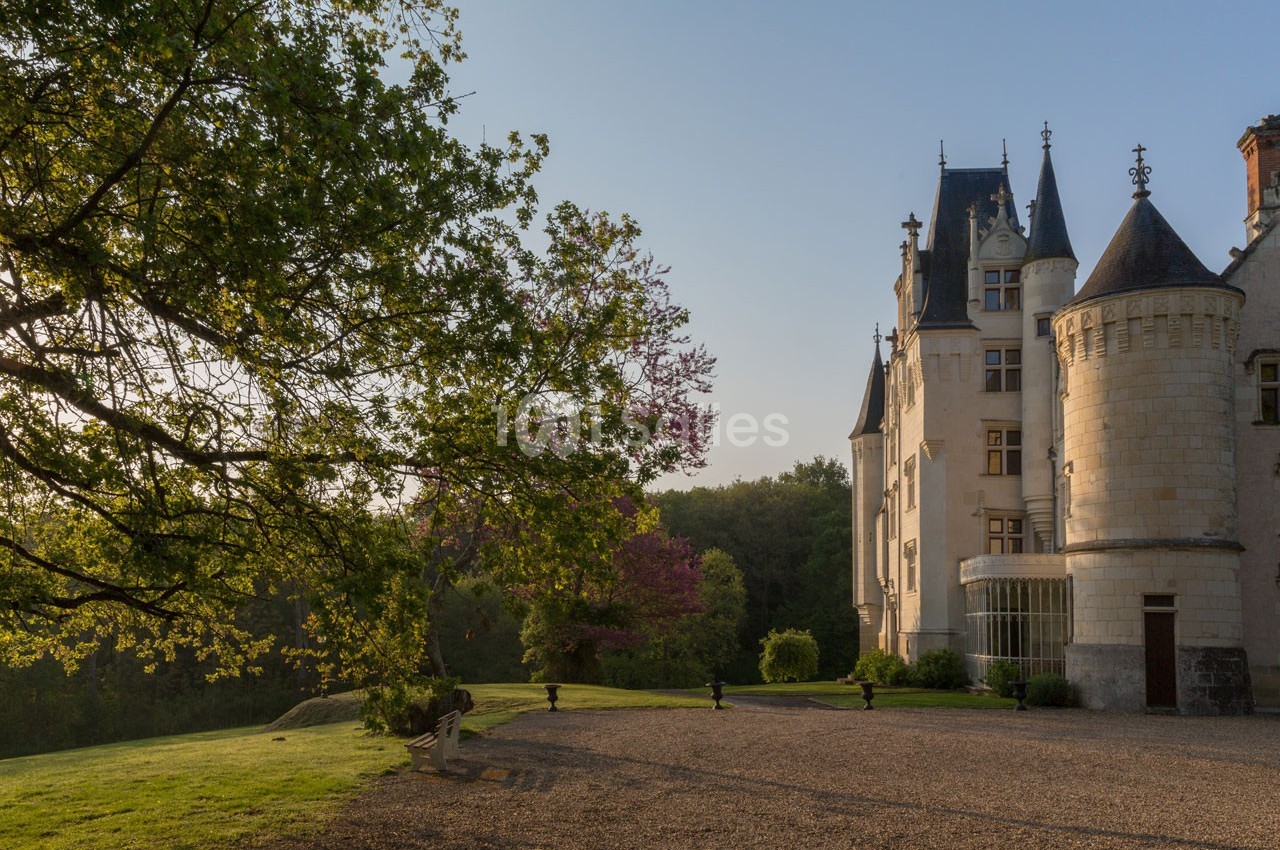 Château historique entouré d'arbres et d'une pelouse, éclairé par une lumière douce en fin de journée.