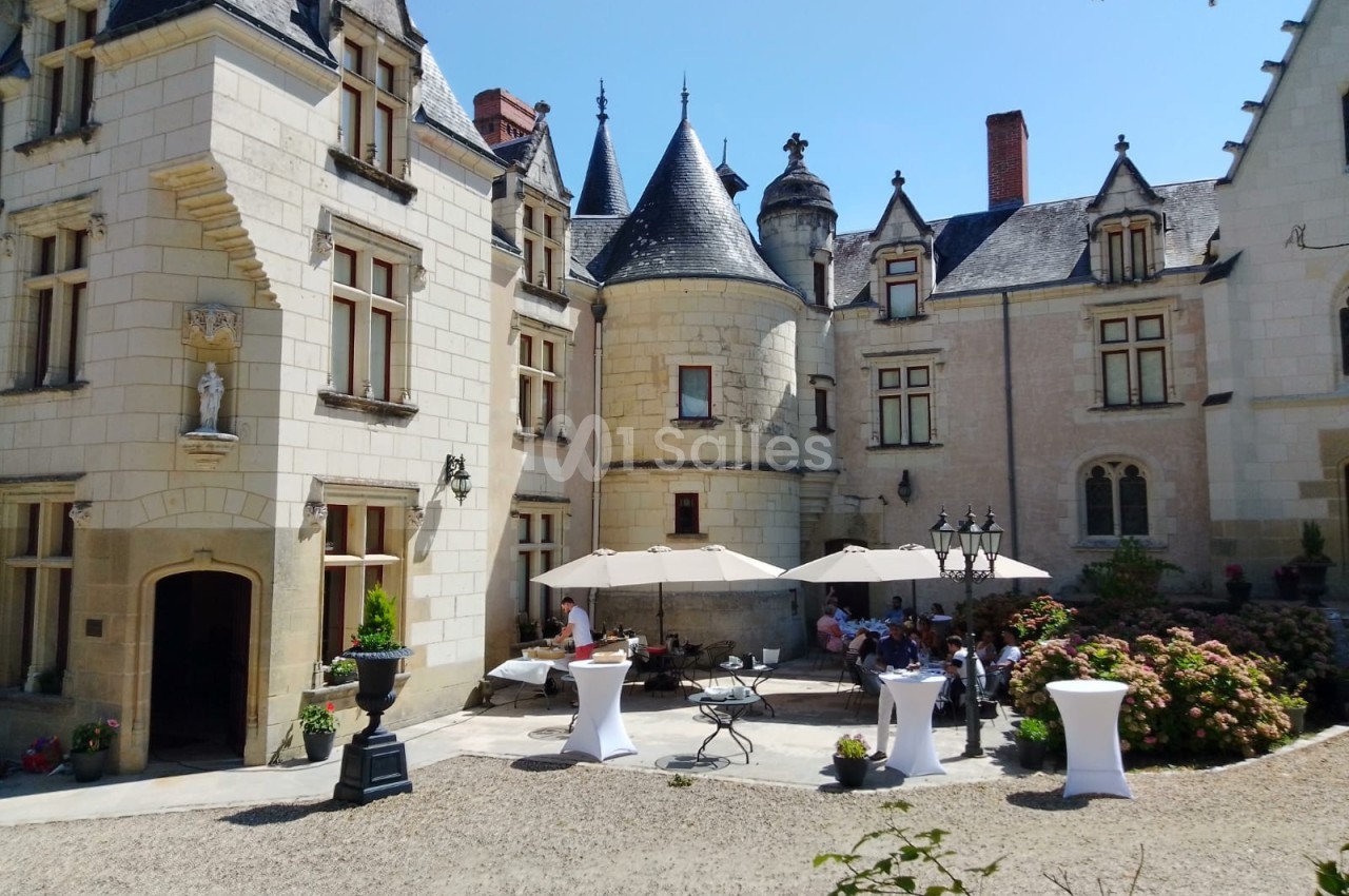 Cour intérieure d'un château avec des tables, des parasols et des personnes réunies par une journée ensoleillée.