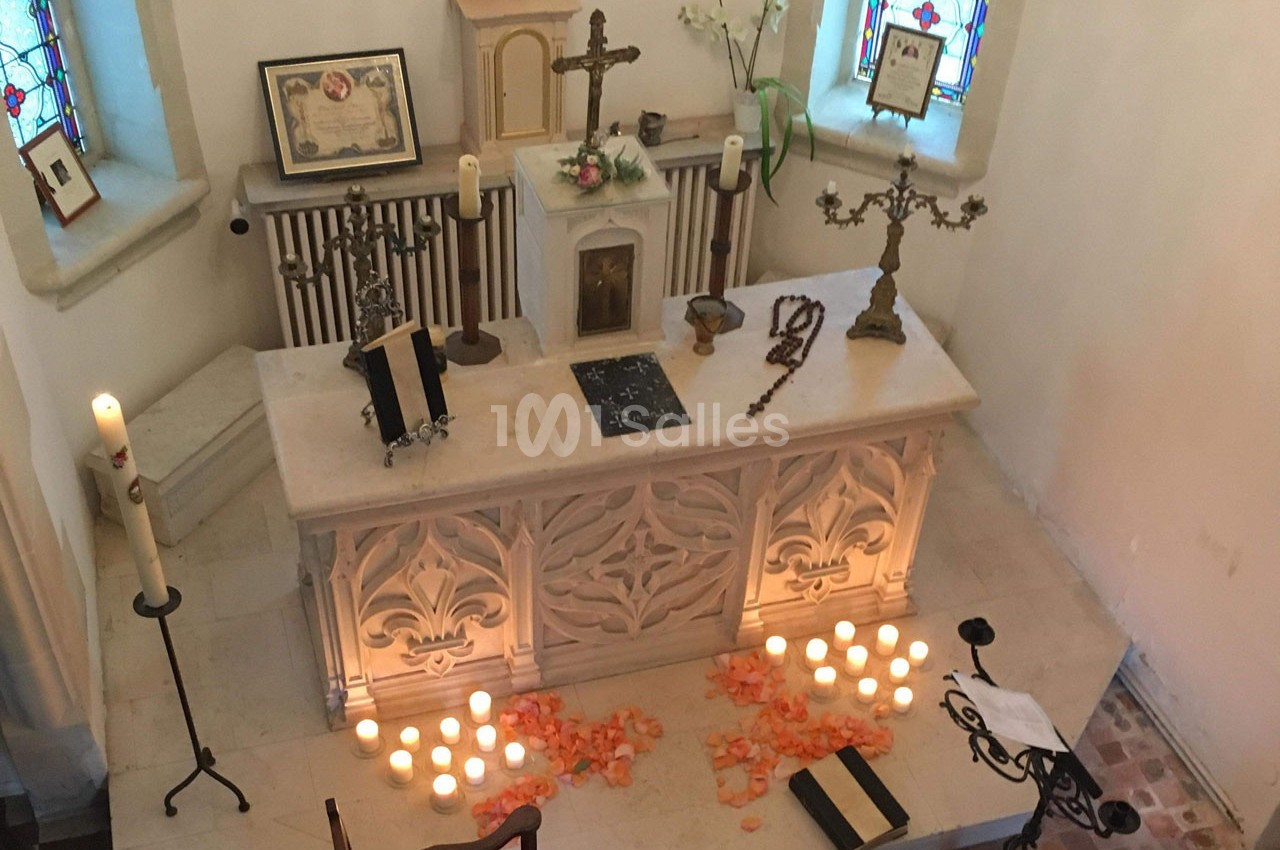 Autel d'église décoré de bougies, pétales de fleurs, croix et objets religieux, entouré de vitraux colorés.