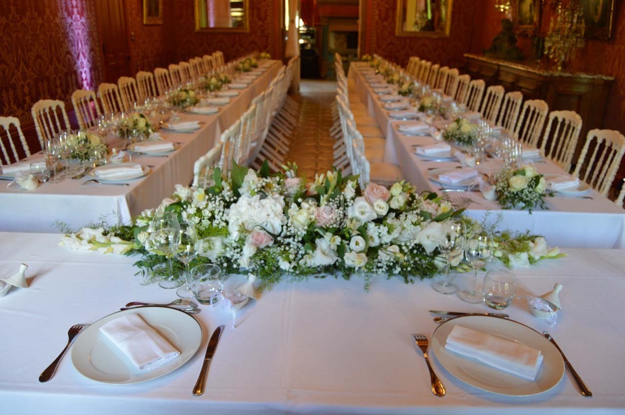 Salle de réception avec tables dressées, nappes blanches, vaisselle élégante et centre de table floral.
