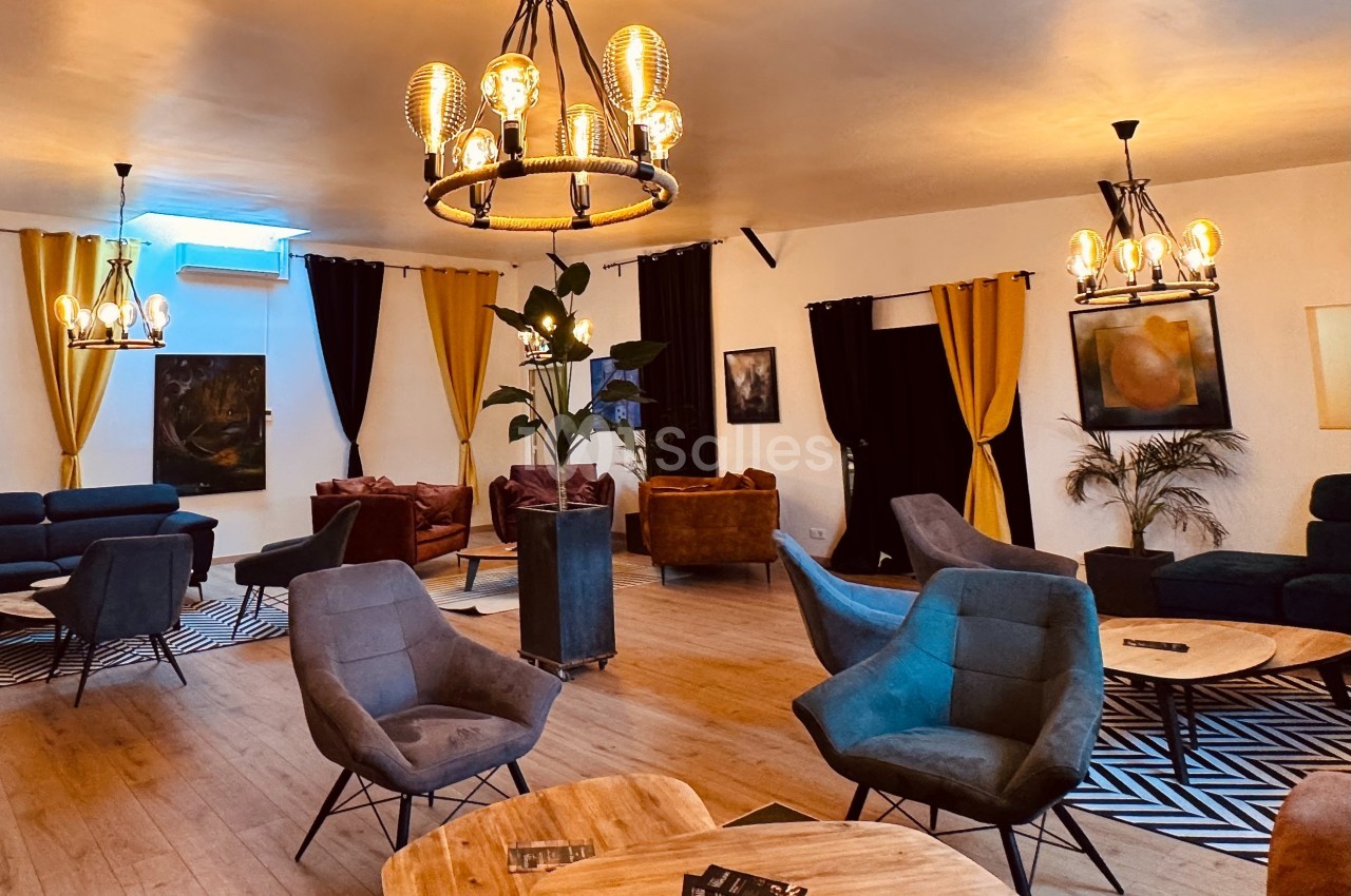 Salle lumineuse avec mobilier moderne, fauteuils confortables, tables basses en bois et éclairage chaleureux.