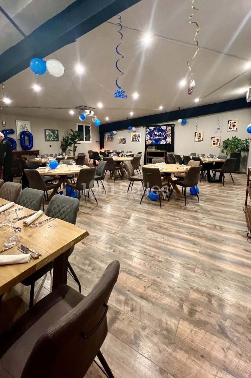 Salle décorée pour une fête avec ballons bleus et blancs, tables dressées et affiches aux murs.